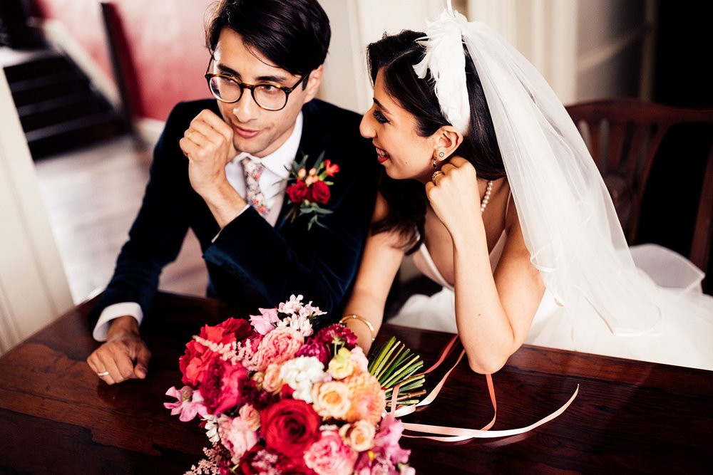 handsome groom in blue velvet suit sits with his bride at legal wedding signing in cotswolds wedding ceremony