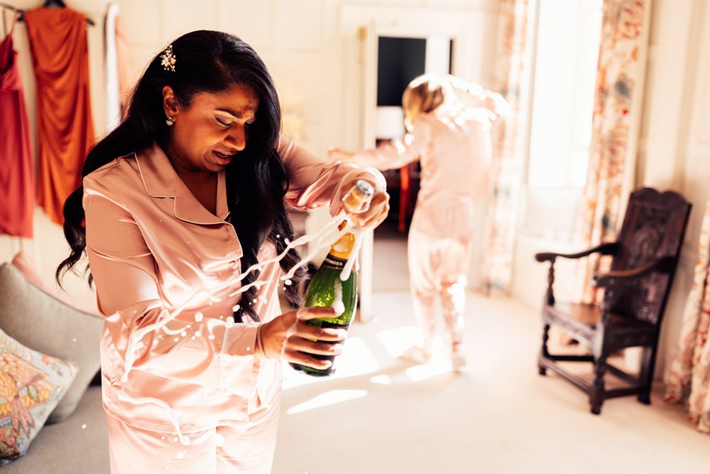 bridemaid in pyjamas pops open champagne and it explodes in beautiful stately home wedding venue