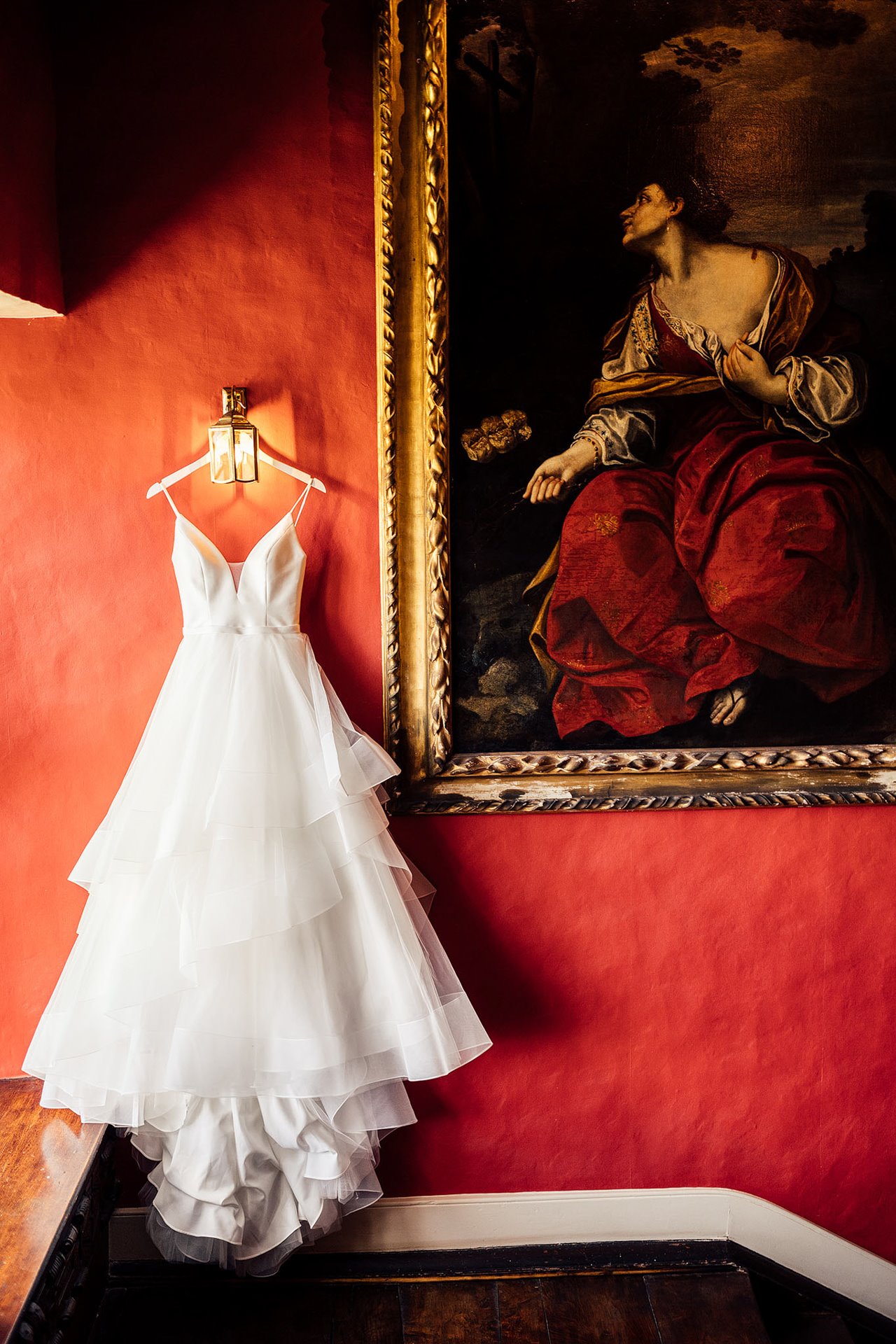 Princess wedding dress hanging on the red walls of stately home elmore court ready for bride to put on
