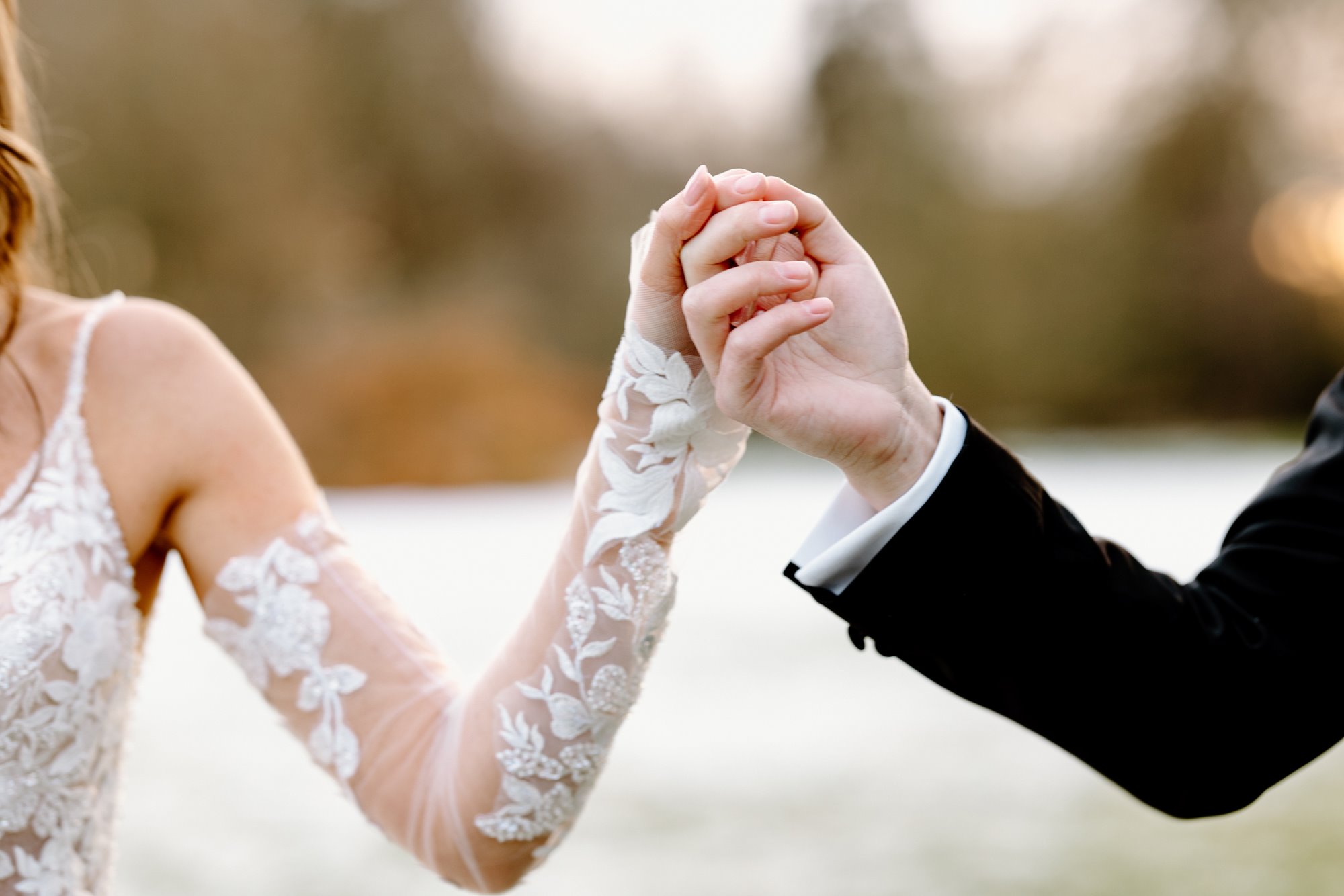 bride wearing lace wedding dress, holding hands with her newly wedded husbands hand in a golden lit meadow