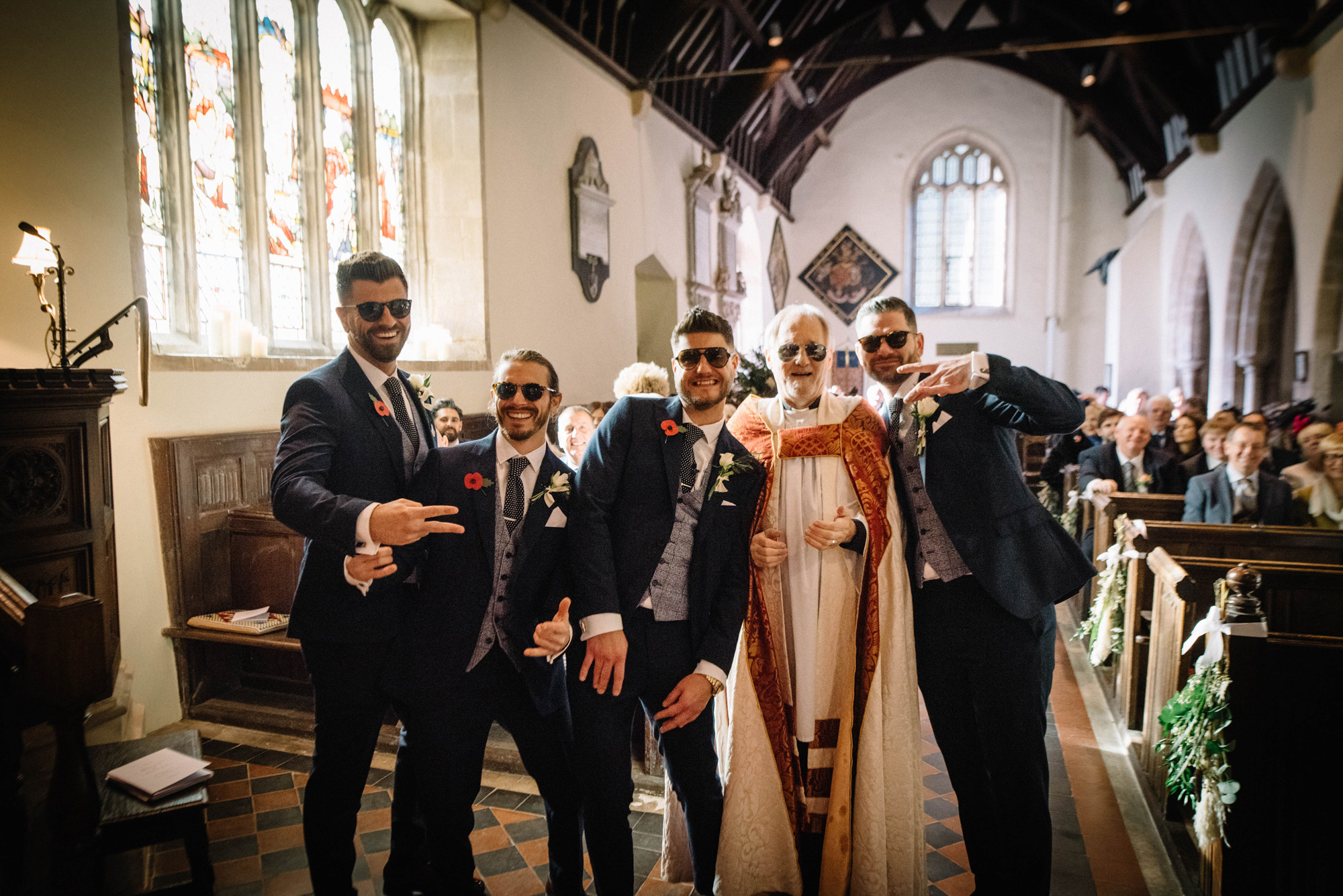 Groomsmen in sunglasses pose with the Vicar of St John the Baptist church at a relaxed church wedding in Elmore