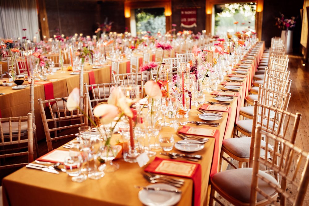 Clashing Colourful fun wedding theme. Orange tables with bright flowers at eco wedding venue in the cotswolds