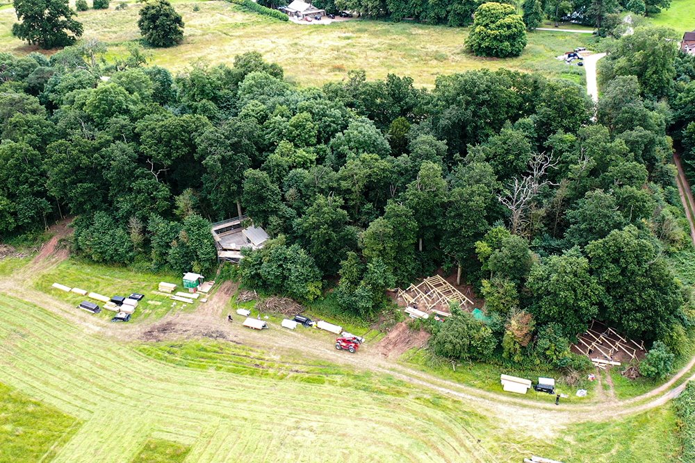 Ariel view of three treehouses being constructed on the border of a woodland which overlooks a stunning field