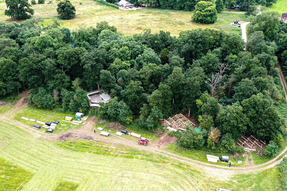 Ariel view of three treehouses being constructed on the border of a woodland which overlooks a stunning field