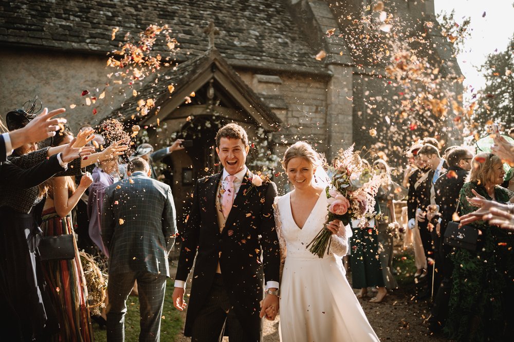 happy couple outside a church after getting married with their friends and family throwing confetti over them