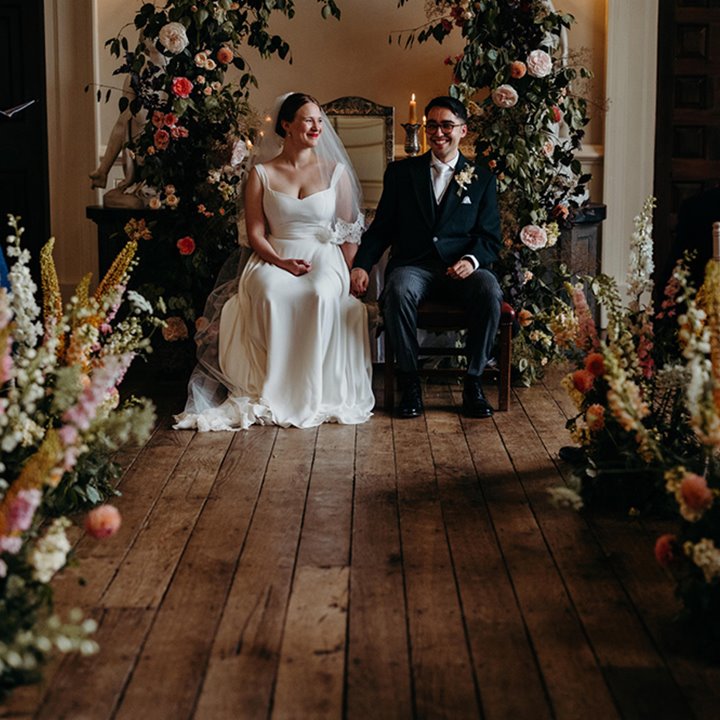 Beautiful newly wed couple sitting in front of a flower arch in the Great Hall at Elmore Court