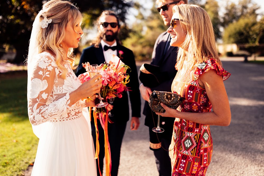 Colourful wedding guests and cool bride and groom in sunny drinks reception outside elmore court