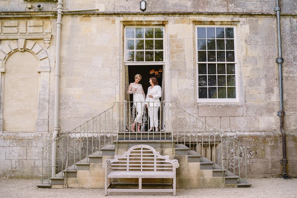 Two brides stand on the steps of stately home wedding venue at their beautiful same sex marriage