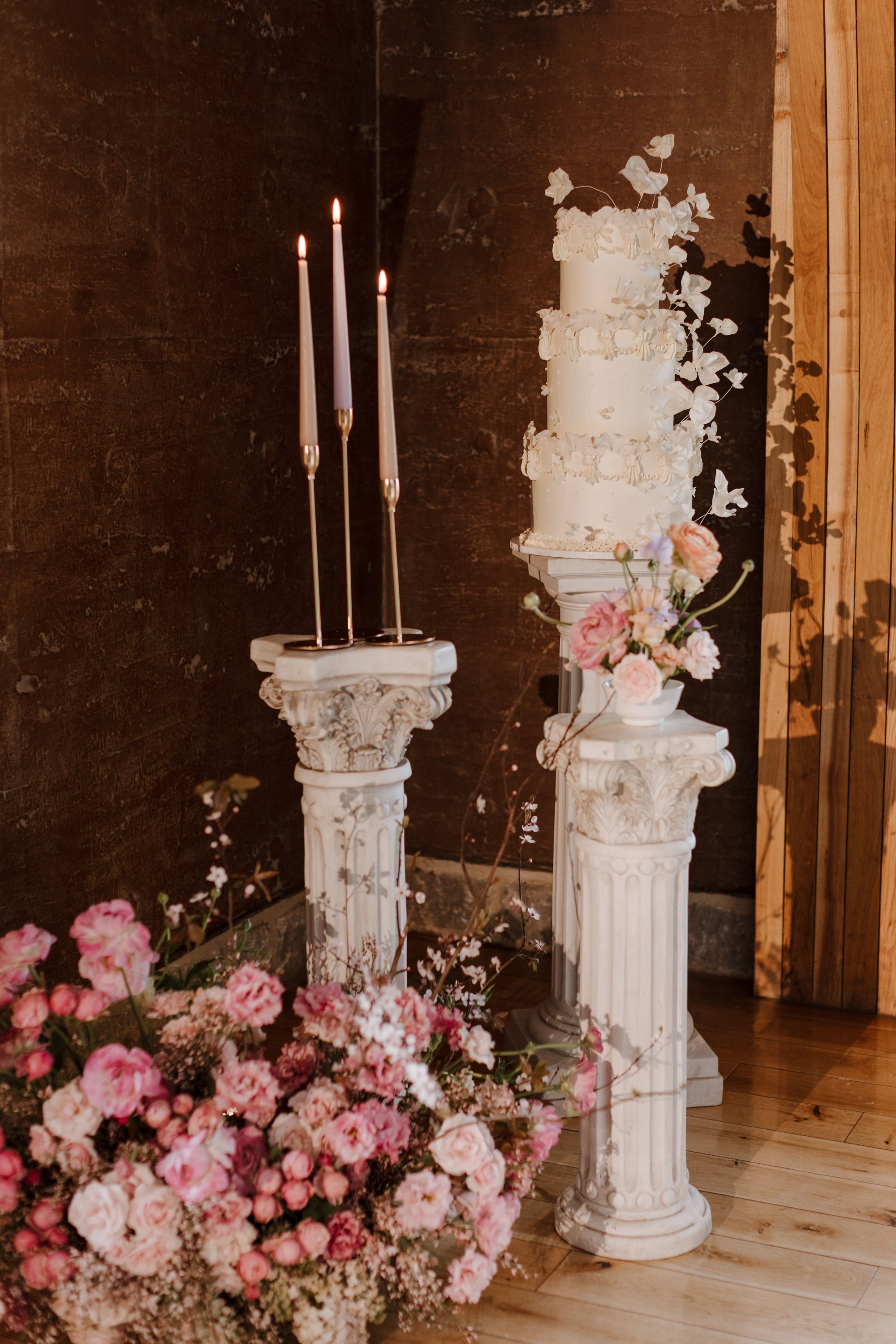 three tiered wedding cake on a roman column with beautiful soft pink flower arrangements at the base