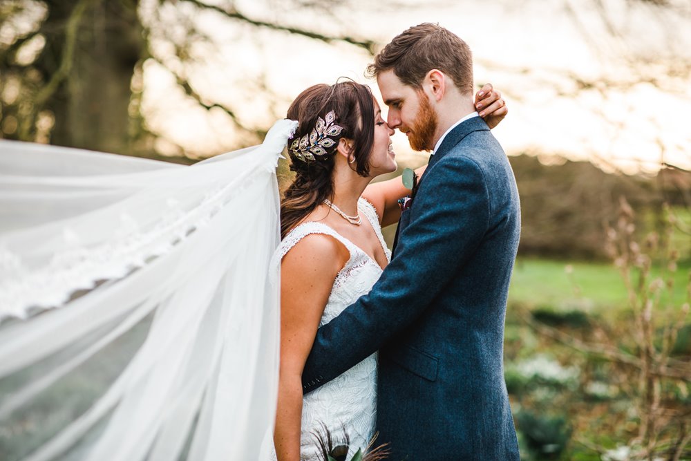 Bride in cathedral veil and headpiece hugging groom outside