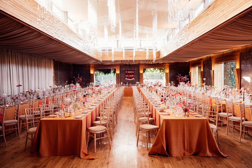 Colourful wedding reception idea: Orange tables with bright flowers at eco venue in the cotswolds