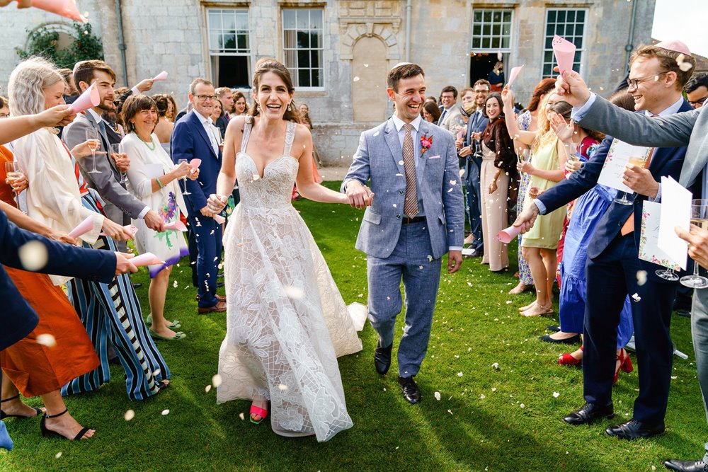 guests throwing colourful confetti on the newly wed couple outside a stately Gloucestershire home