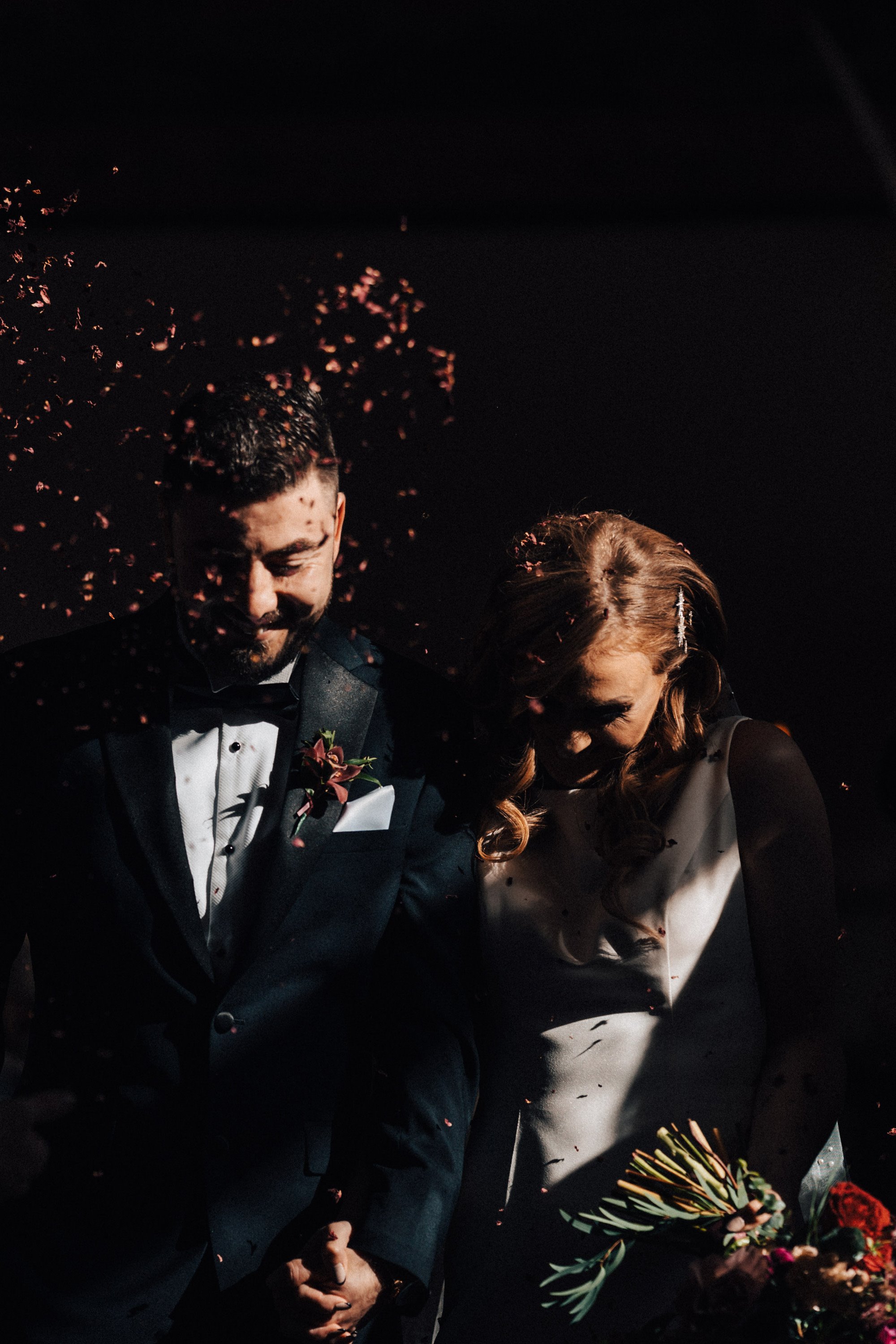 Moody photo of bride and groom confetti being thrown at faces in atmospheric october wedding 