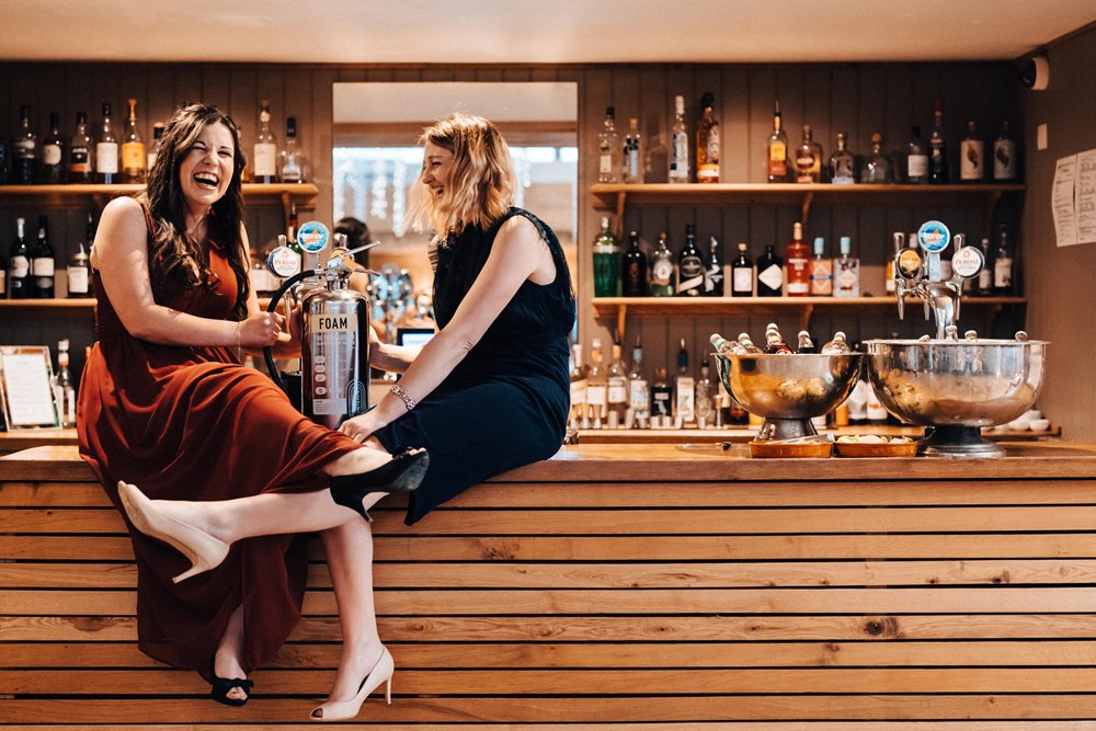 Fun bridesmaids sit on the bar at a Relaxed winter wedding in the cotswolds