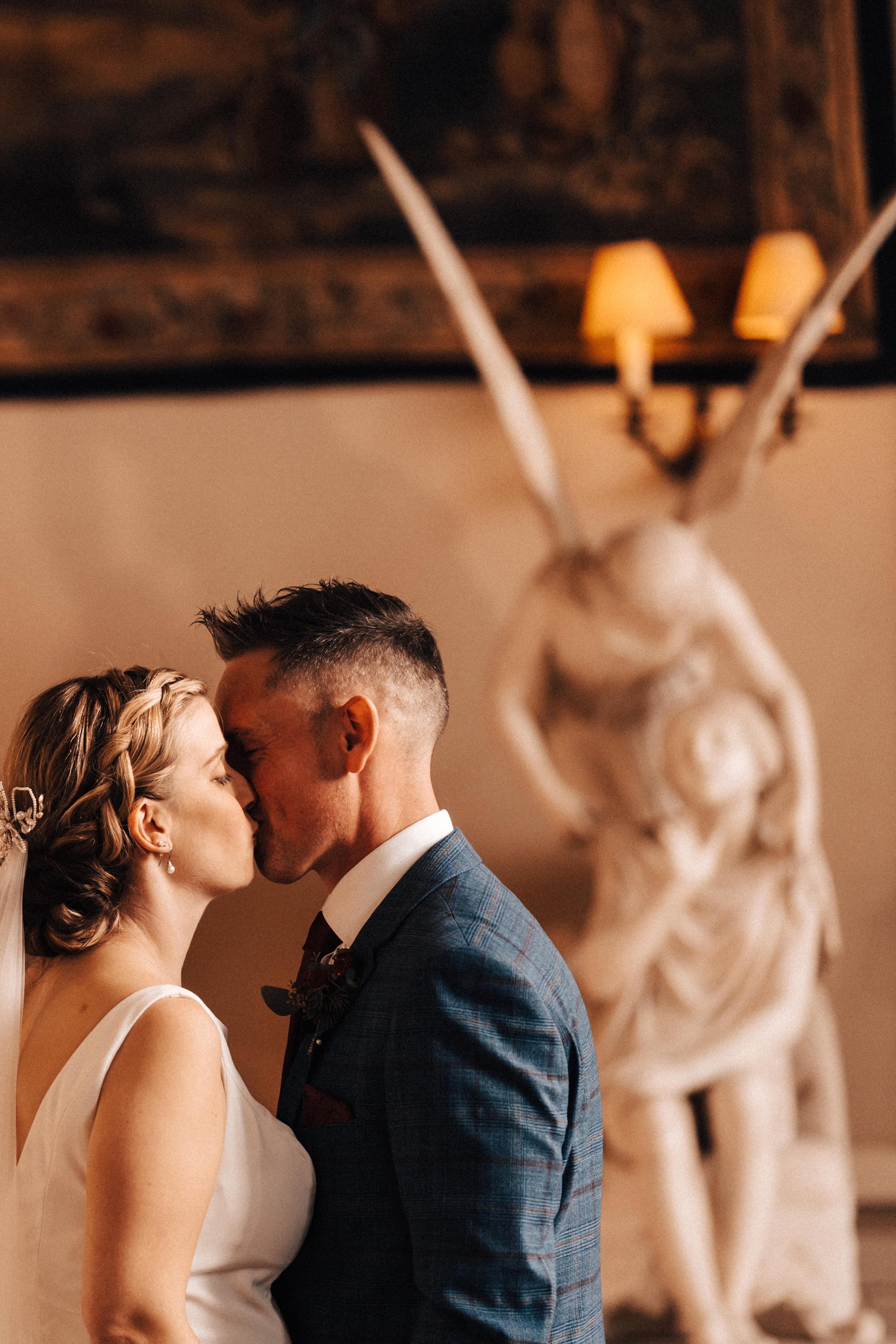 bride and groom kiss in front of angel statue at their christmas wedding ceremony in stately home