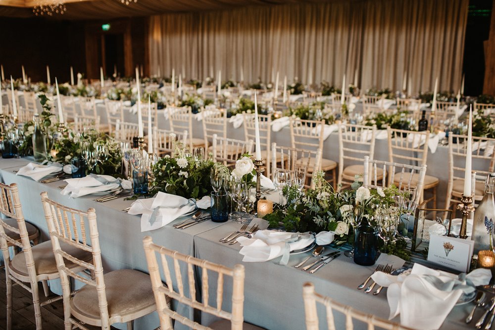 Natural wedding colours in 2021. Banquet tables decorated with greenery, grey linen and white candlesticks