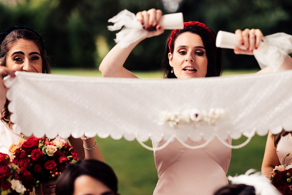 Bridesmaid sprinkles sugar onto silk veil at persian ceremony outside stately home elmore court in the cotswolds