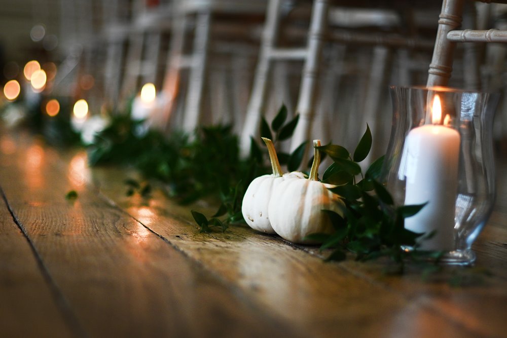 Pumpkin wedding aisle with candles and greenery for a homegrown halloween wedding in an old manor house in england