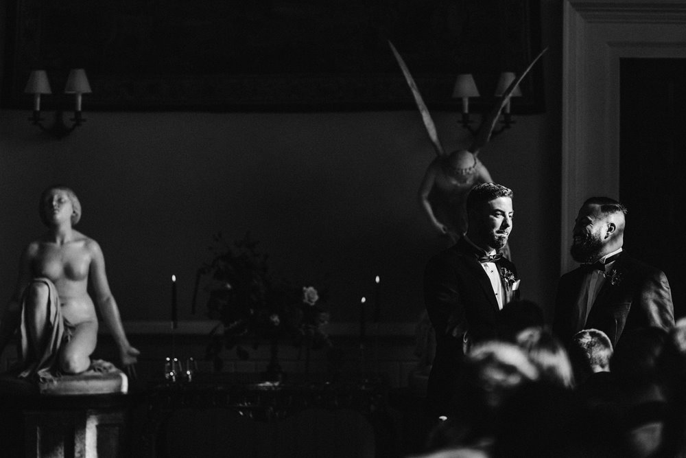 moody wedding photo of groom waiting for bride next to angel statues in ceremony room at stately home elmore court for an autumn wedding