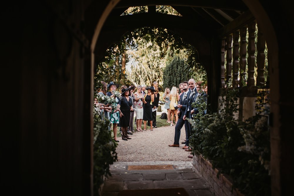 Beautiful church doorway looks out to guests waiting to throw confetti at a wedding in the uk