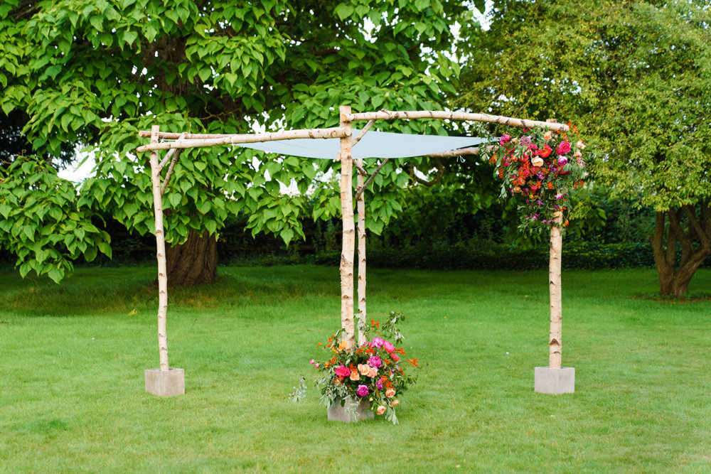 Wedding chuppah decorated with pink and orange flowers in the gardens at stately home elmore court