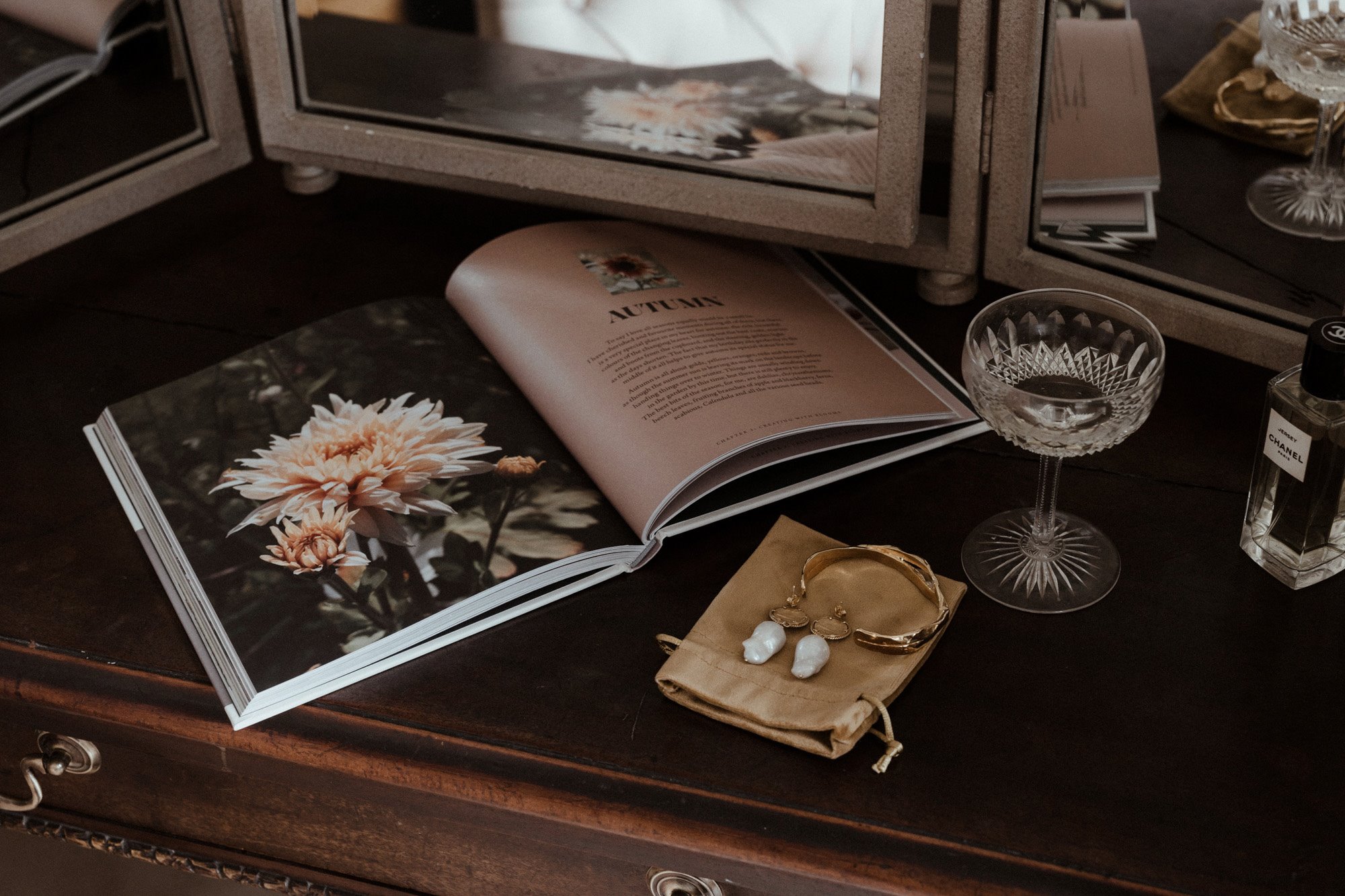 Eco wedding shoot with wild flower magazine and pearl earrings and champagne glass laid out on dressing table 