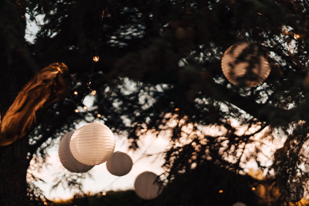 Lanterns and fairy lights hanging in cedar tree branches with sunset sky behind for an enchanted October wedding in the cotswolds