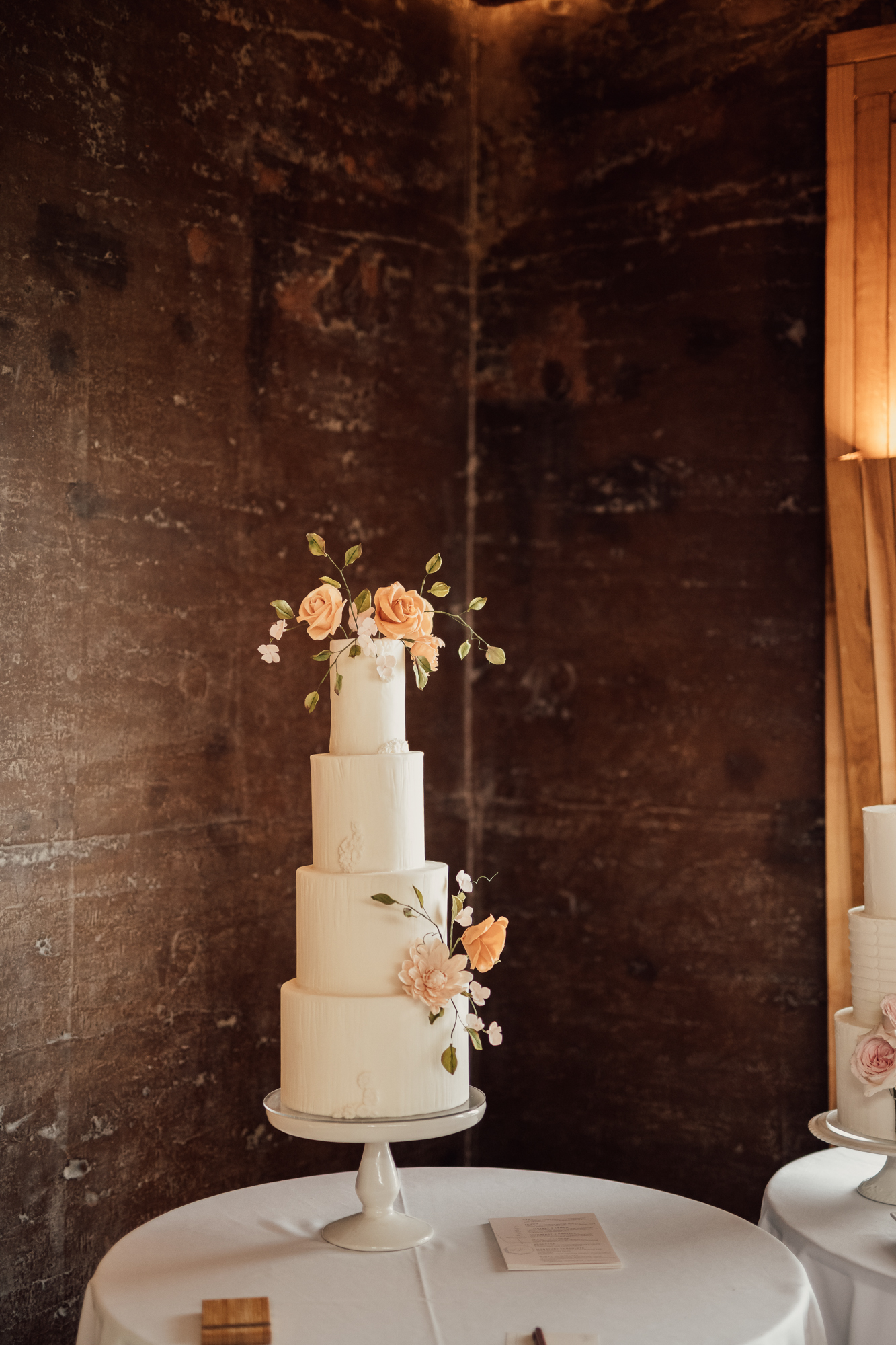 Elegant wedding cake in front of the rammed earth wall of eco wedding reception venue at Elmore Court in Gloucestershire