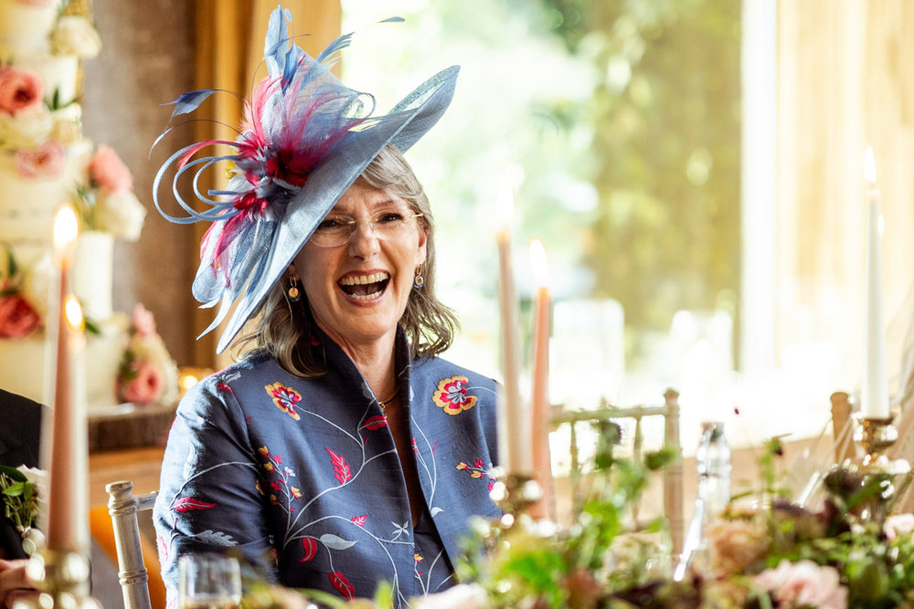 Beautiful mother of the bride laughing with blue and purple hat and stunning matching outfit in a unique indian material by Shibumi