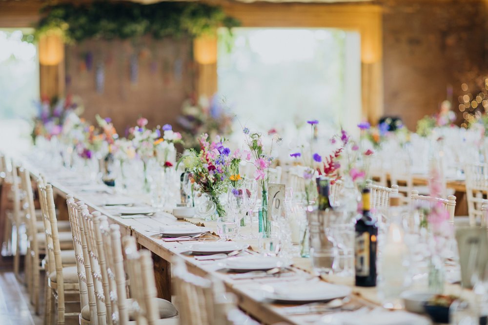 wild wedding flowers on long tables decorating a reception at eco wedding venue in the cotswolds