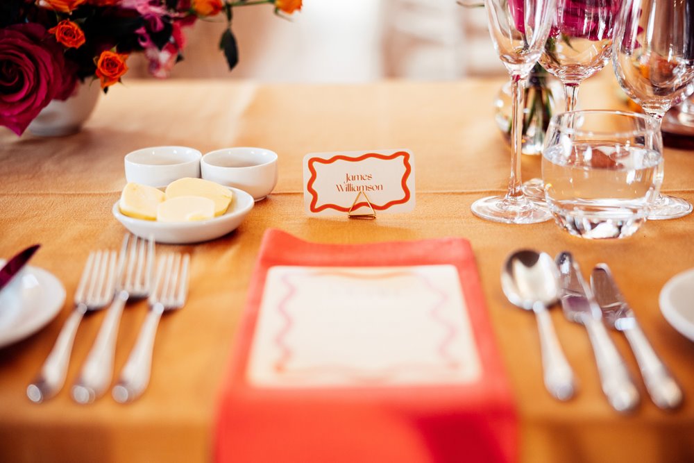 Colourful wedding reception. Clashing Orange colour scheme with bright flowers at eco venue in the cotswolds