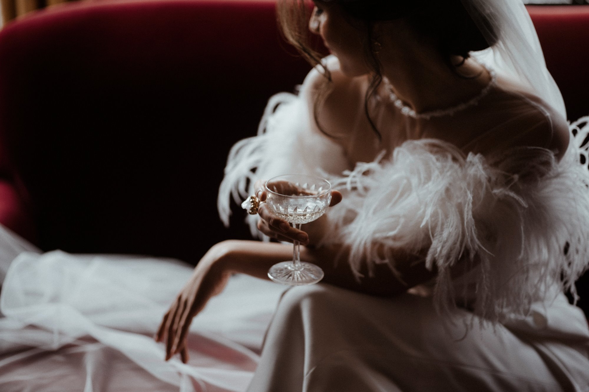 bride wearing a feather boa holding a glass of champagne while posing in a dark and moody shot