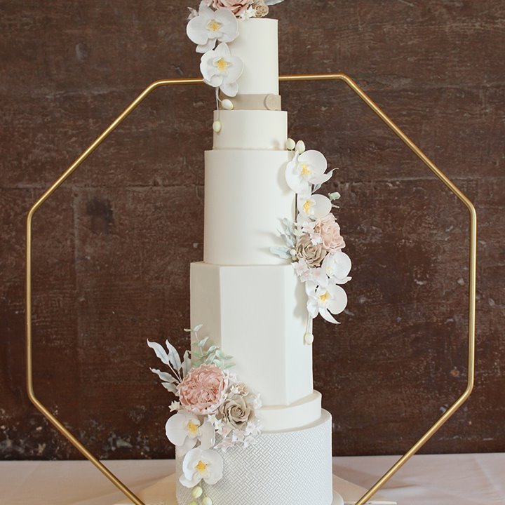 Extra tall 5 tier luxury modern wedding cake with white icing and different shaped layers decorated with pale pink and white flowers at elmore court