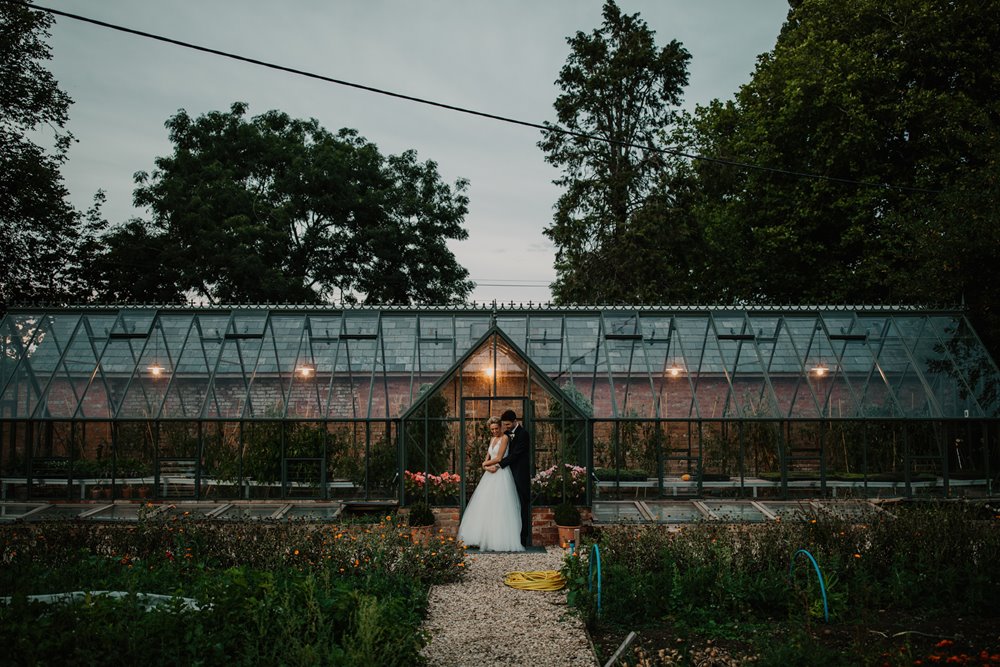 bride and groom pose for couple shots in front of the beautiful glass house at their Walled garden wedding in the cotswolds