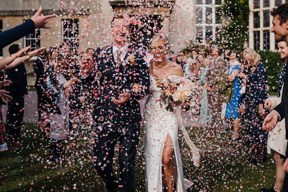 guests throwing colourful confetti on the newly wed couple at Elmore Court