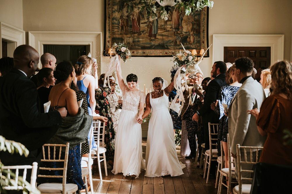 Two happy brides walk down the aisle as mrs and mrs at stately home wedding venue elmore court in the cotswolds