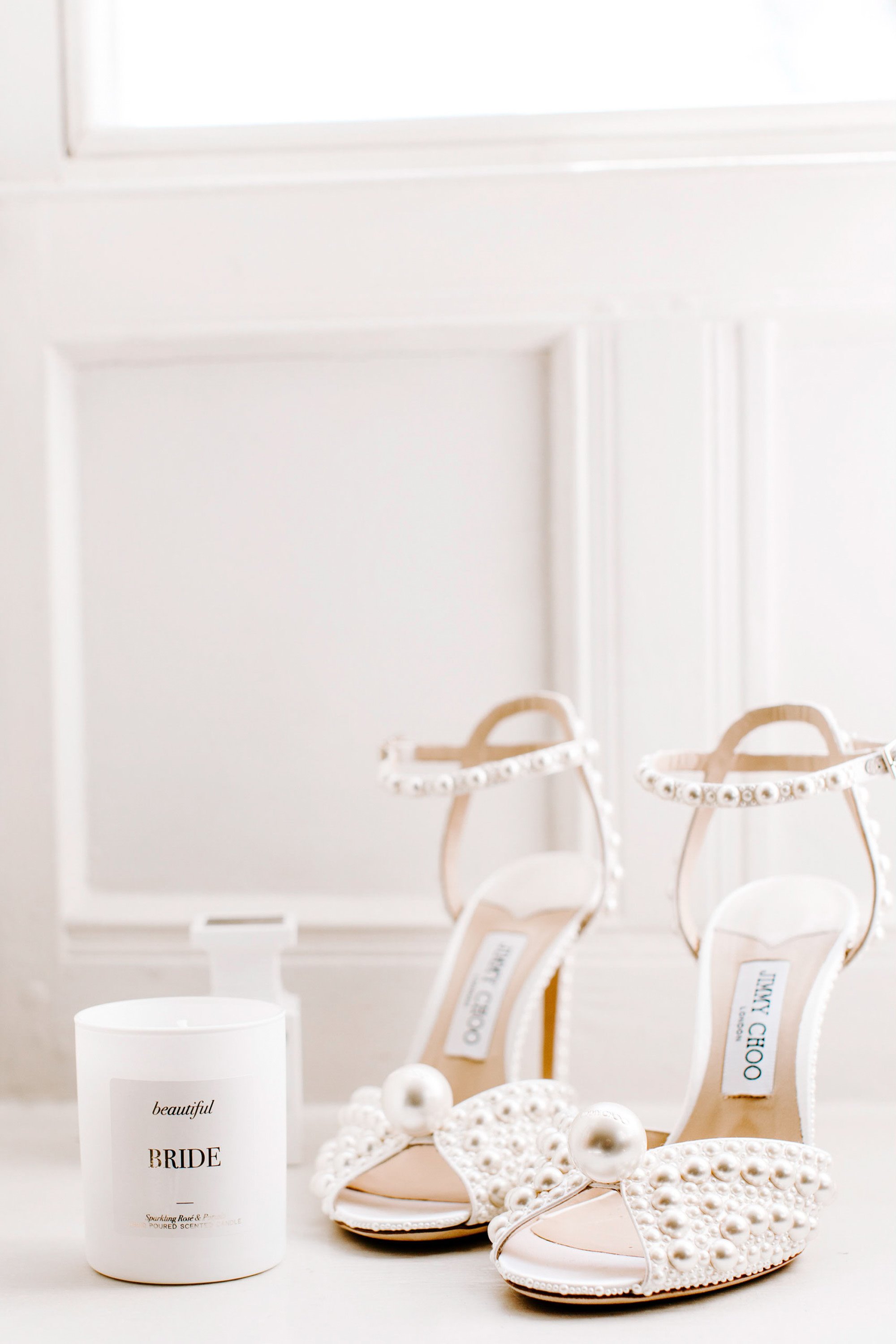 Glamorous Jimmy choo pearl bridal heels with all over pearls and large pearl on toe next to bridal candle on white wooden windowsill
