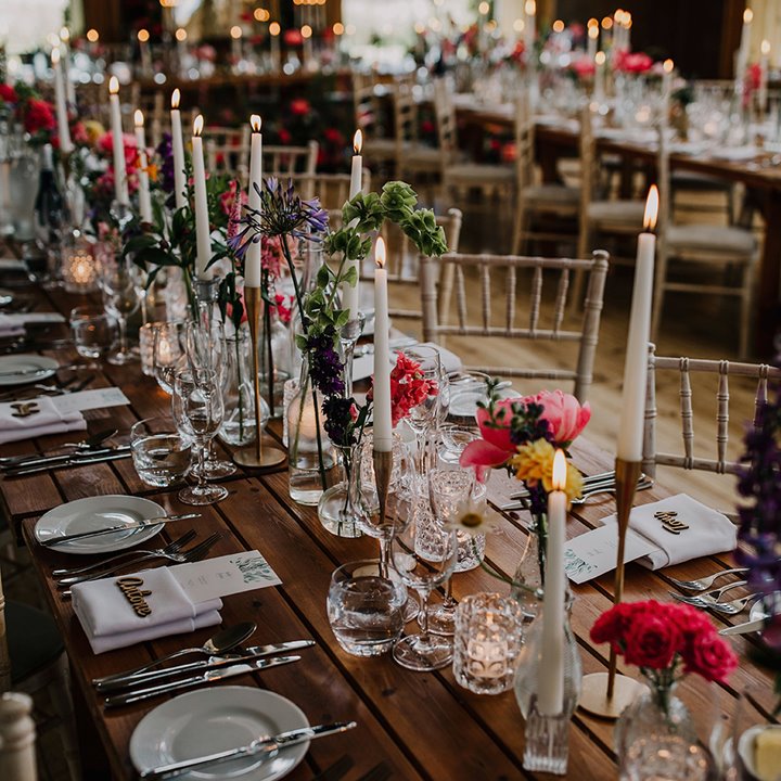 Pretty candlelit wedding reception with pink flowers on long wooden tables and gold candlesticks and tea lights in lots of glassware 