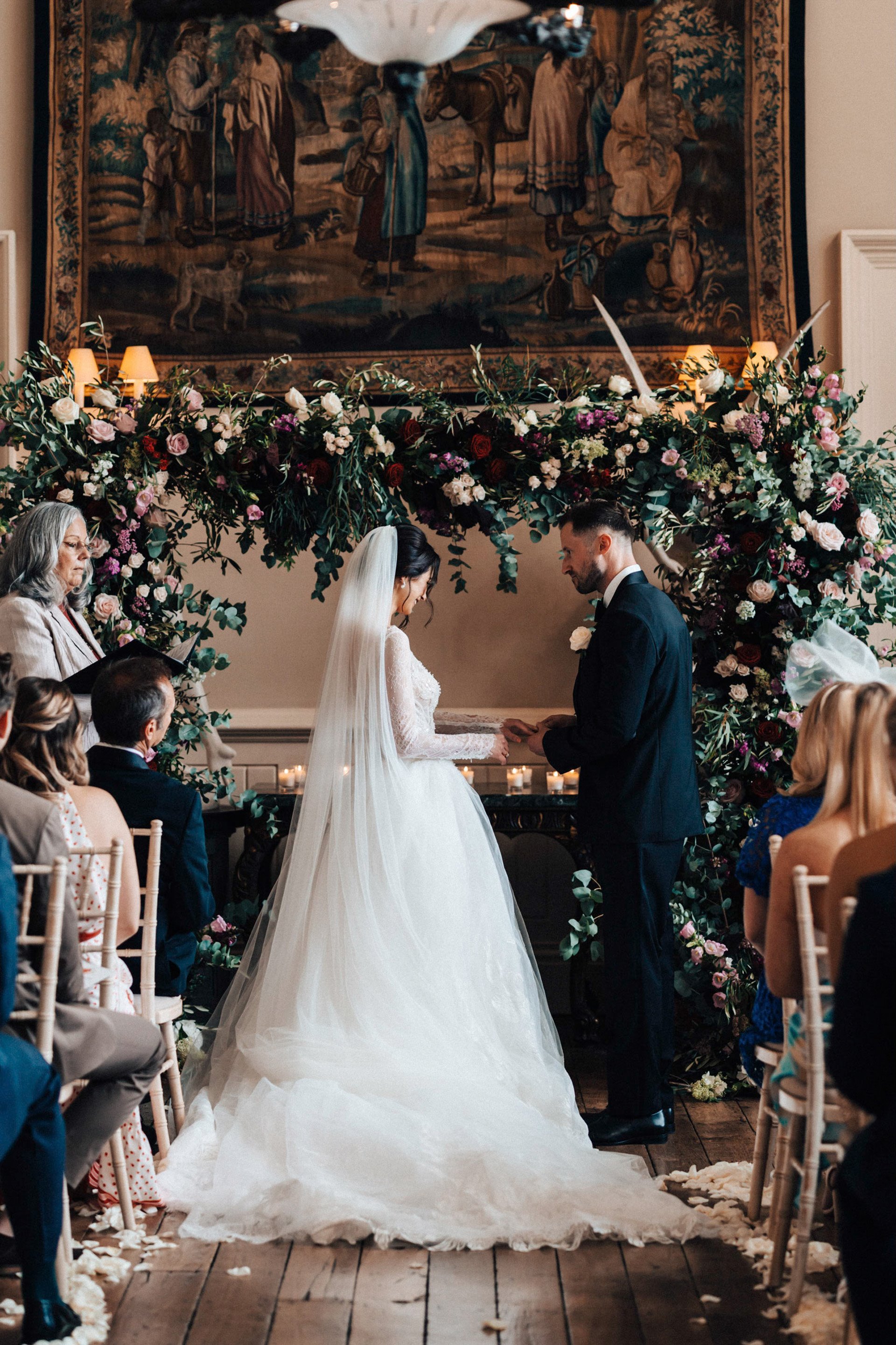 Bride in long veil and groom hold hands in front of Wedding ceremony arch of real flowers at romantic wedding ceremony in mansion house elmore court