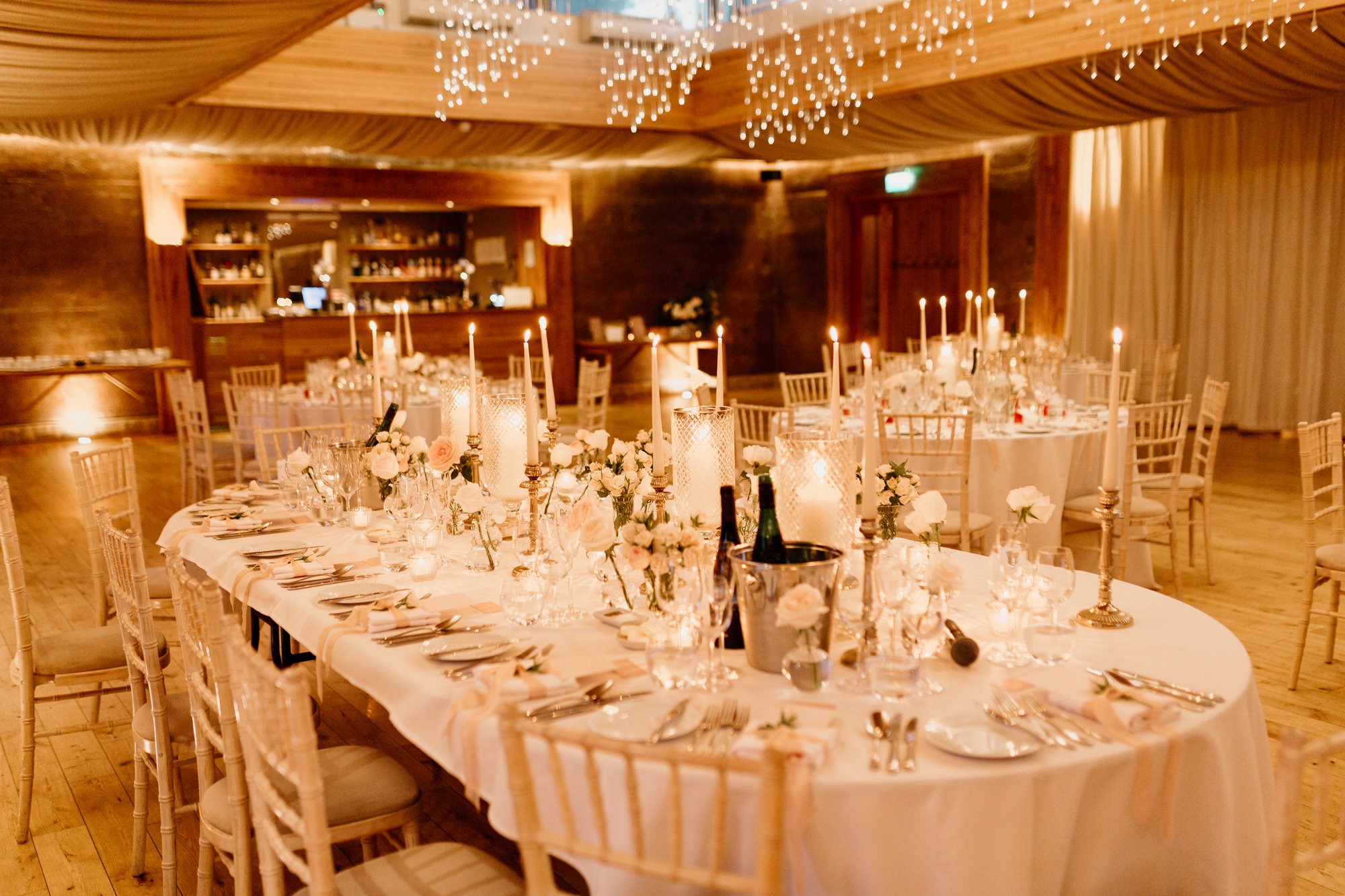 candle lit wedding reception with tables dressed with flowers, white linen and crockery