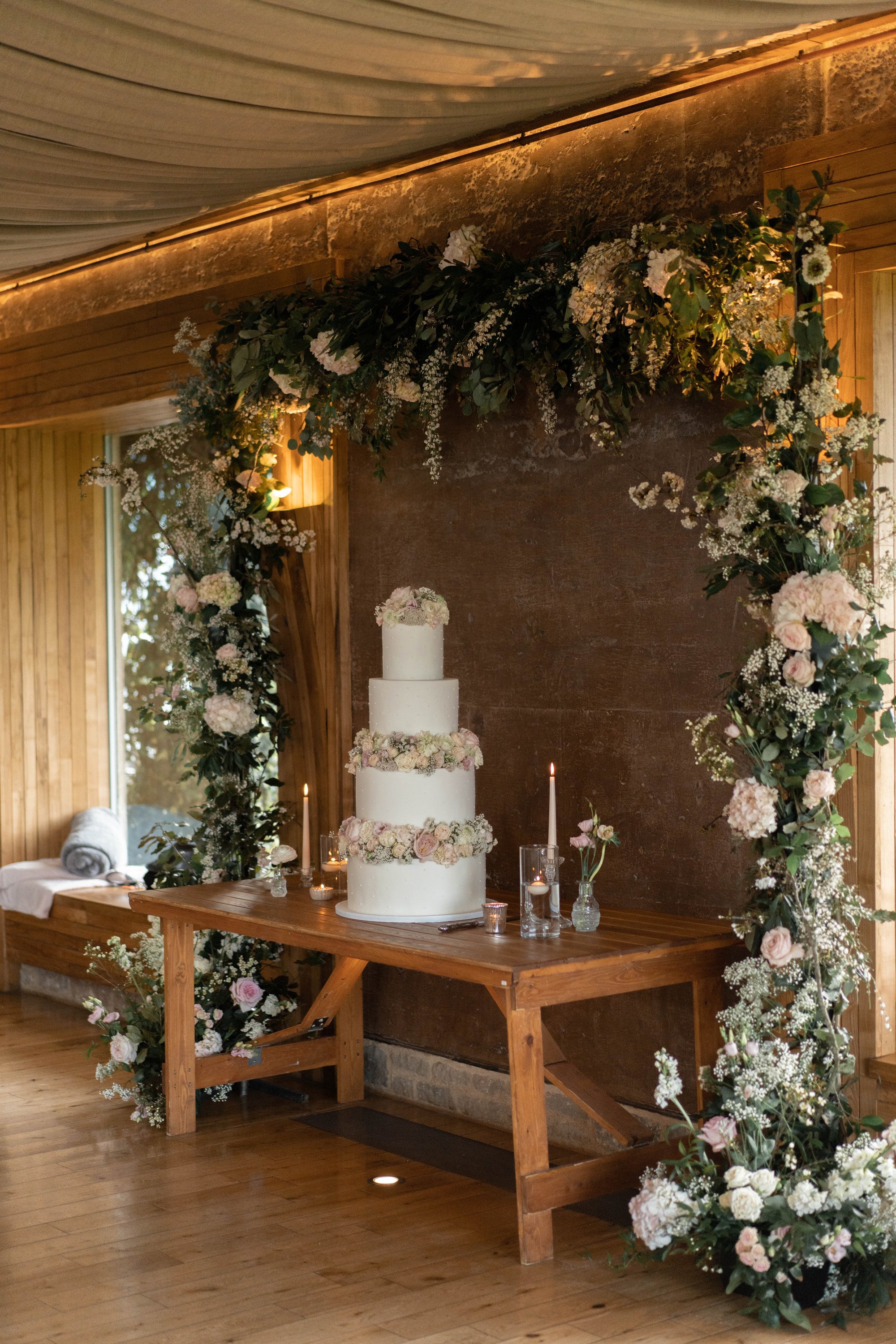 Pearl theme wedding with a three tier cake decorated with pearls and a floral arch with roses