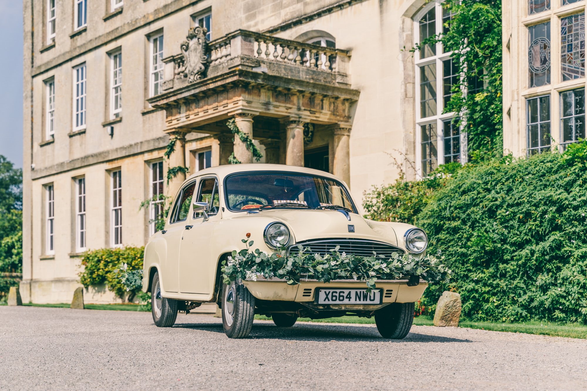 Vintage ambassador car decorated with foliage in front of mansion house elmore court for a garden party wedding
