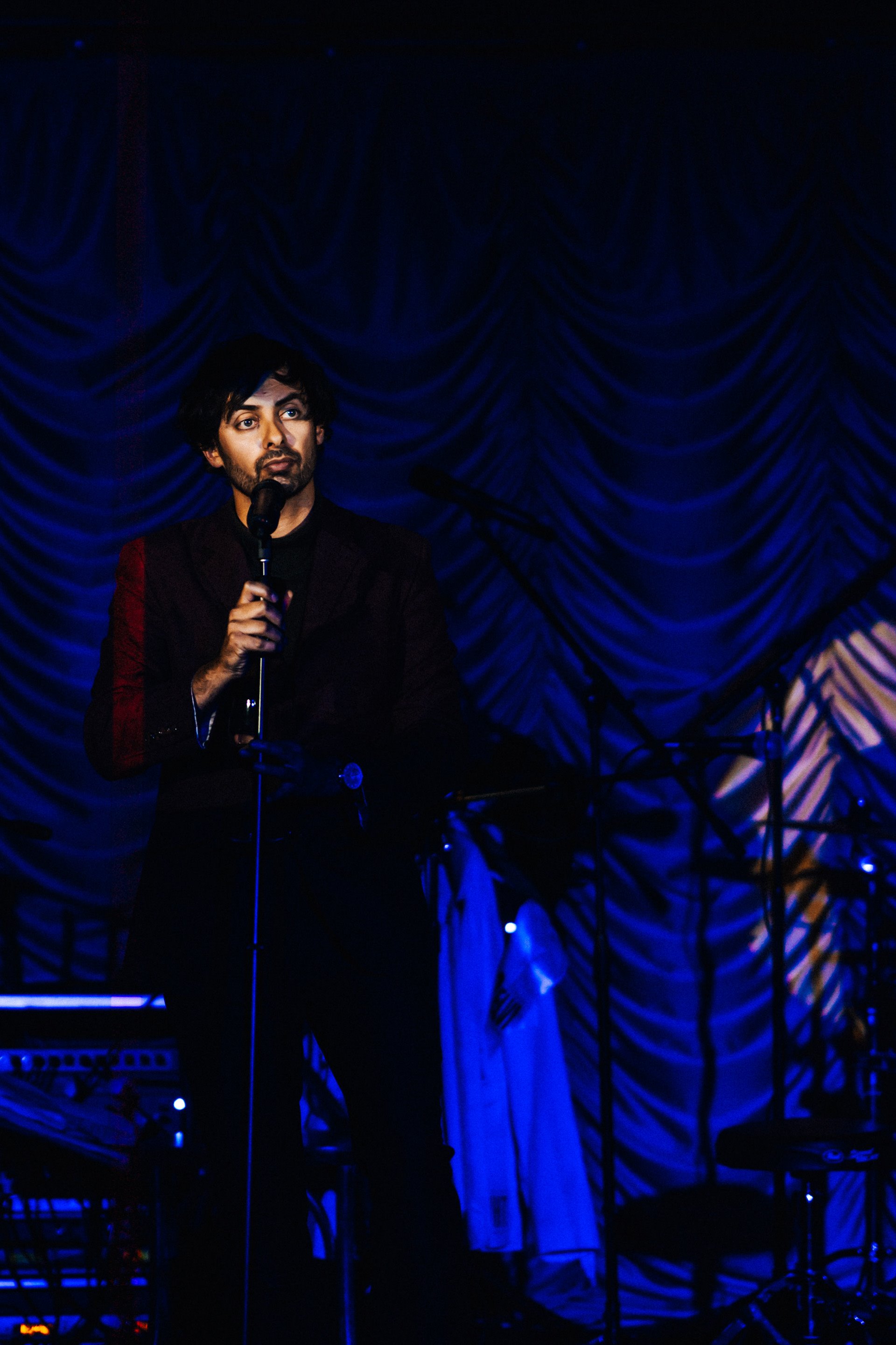Dry stand up comedian Marcel lucont looks blankly at the audience in a purple suit and bare feet on stage at a cabaret dinner