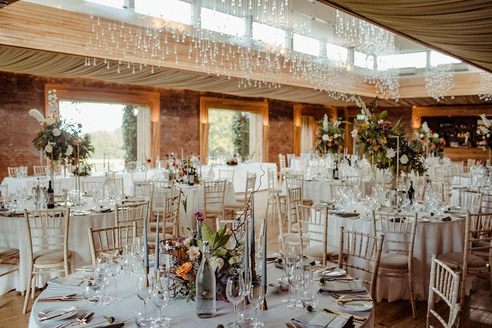 Autumn wedding reception with round tables and gold cutlery in a beautiful light and airy venue with twinkling light shower