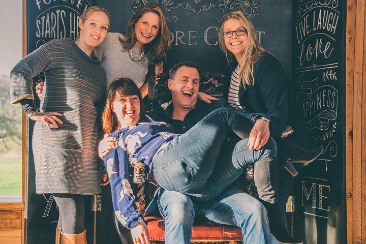 Anselm Guise with Team E member on lap laughing at Elmore Court wedding fair in Gloucestershire
