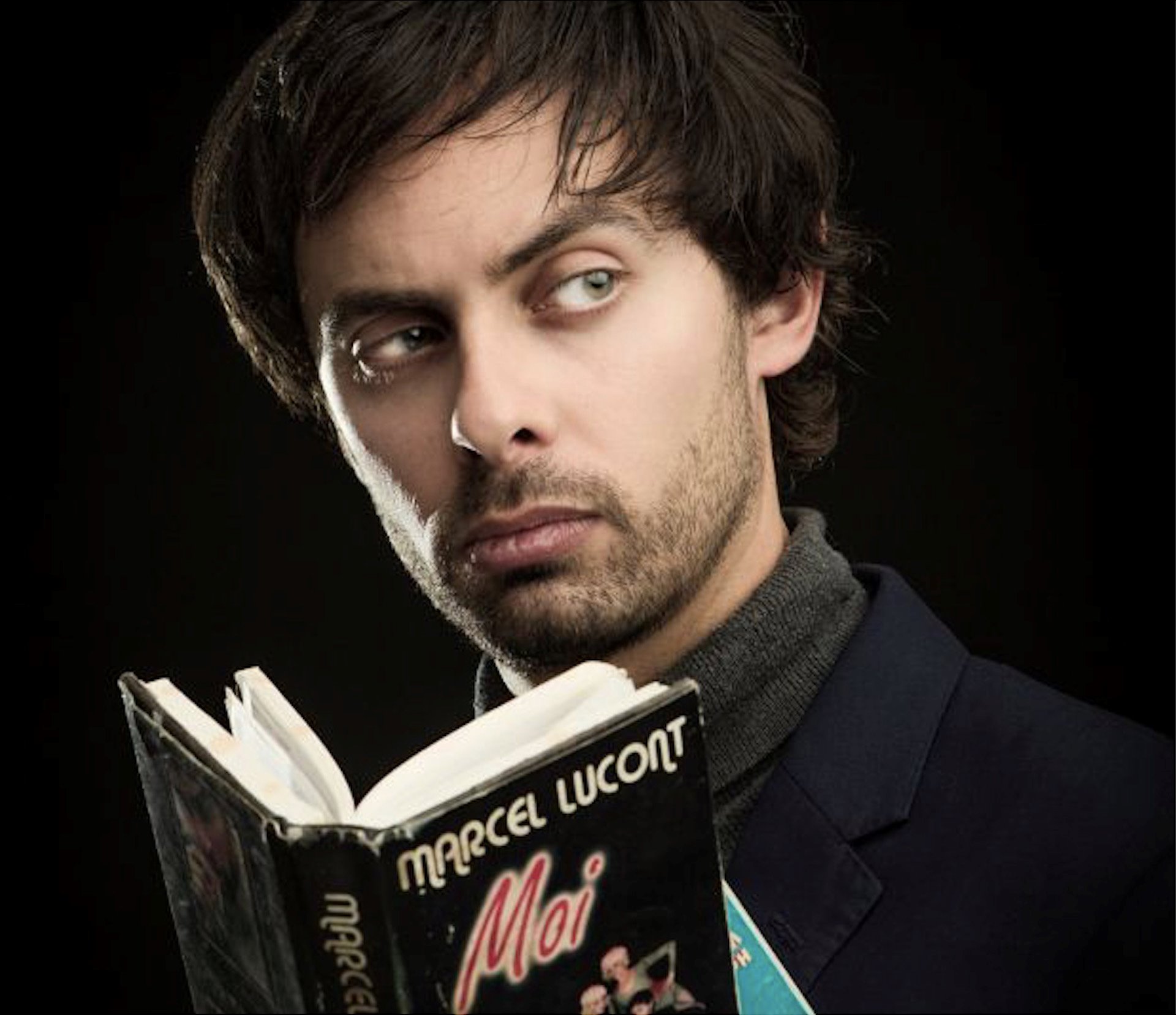 French comedian Marcel Lucont peers over the top of a book with his name on the cover for a cabaret dinner show in the cotswolds