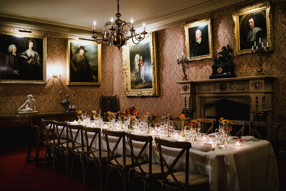 Intimate wedding dining table in a historic house with family portraits and red wallpaper