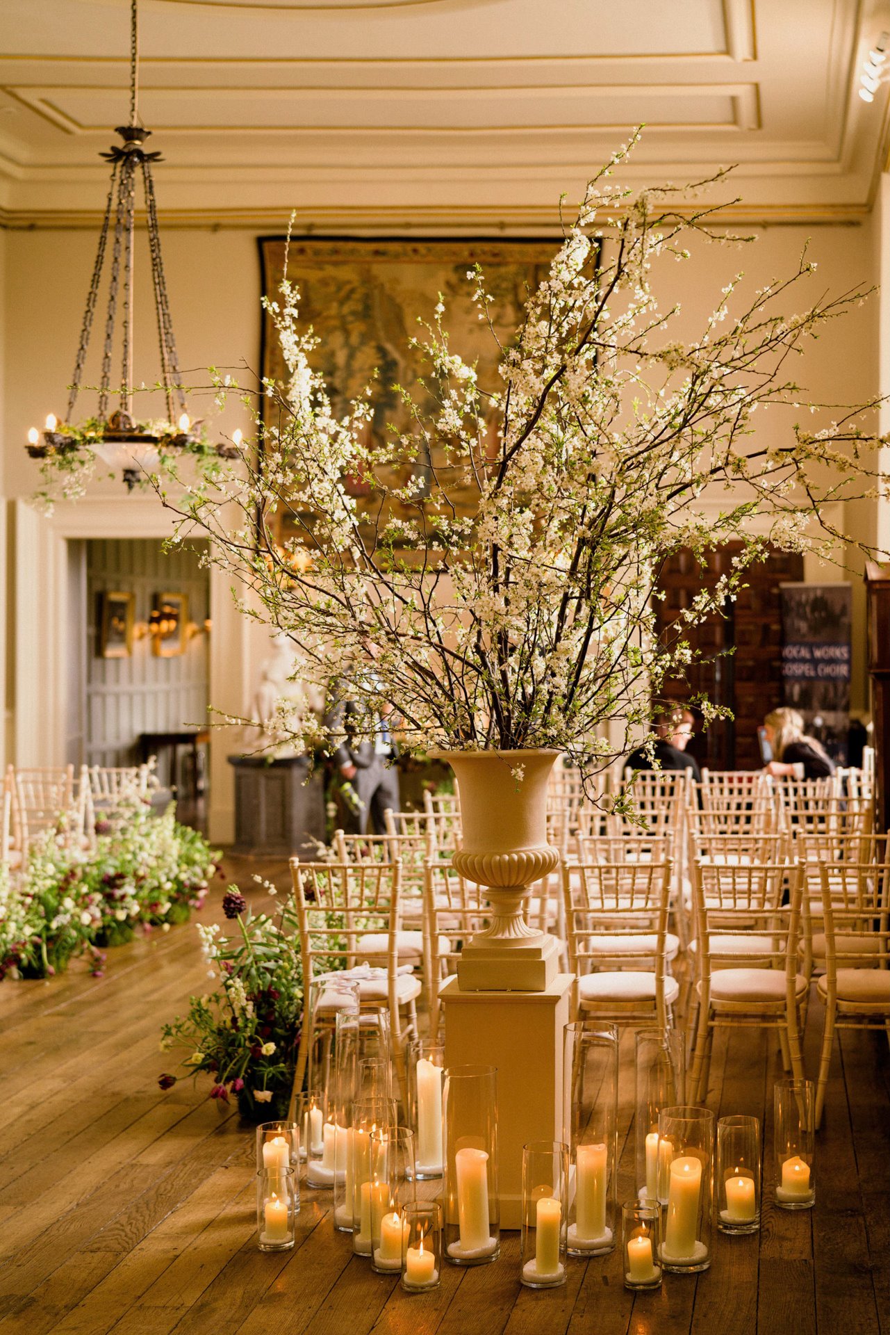 Wild styling of the hall in stately home elmore court with blossom branches, wildflower aisle and candles in hurricane lanterns for March wedding fair