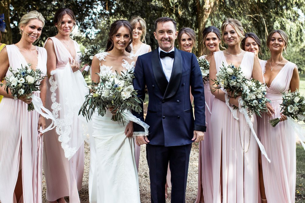 Bride and groom and bridal party pose with bouquets in the prettiest churchyard in England at Elmore Church