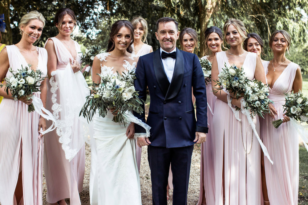 Bride and groom and bridal party pose with bouquets in the prettiest churchyard in England at Elmore Church